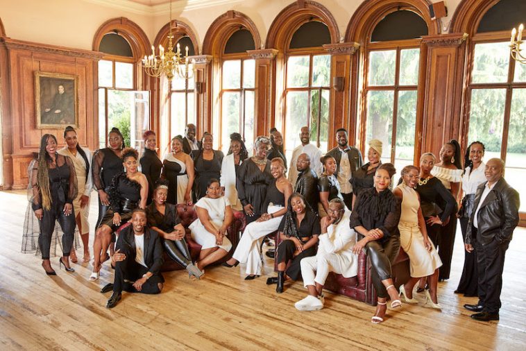 Promotional photo for "Not Giving Up" which sees The Kingdom Choir gathered together in a hall with floor-to-ceiling arched windows behind them.