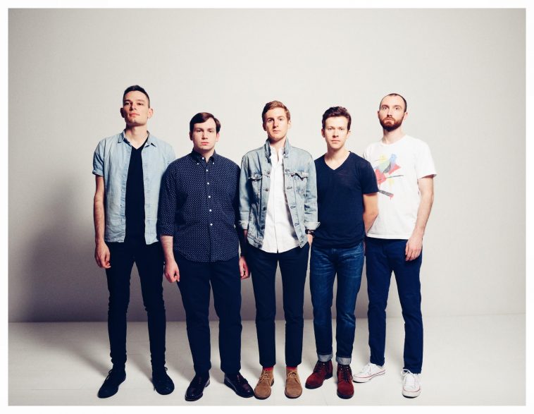 Promotional photo for "Desert Bloom" which sees Earthquake Lights posing in a professional photo studio, where all five band members are lined up, all wearing jeans and shirts.