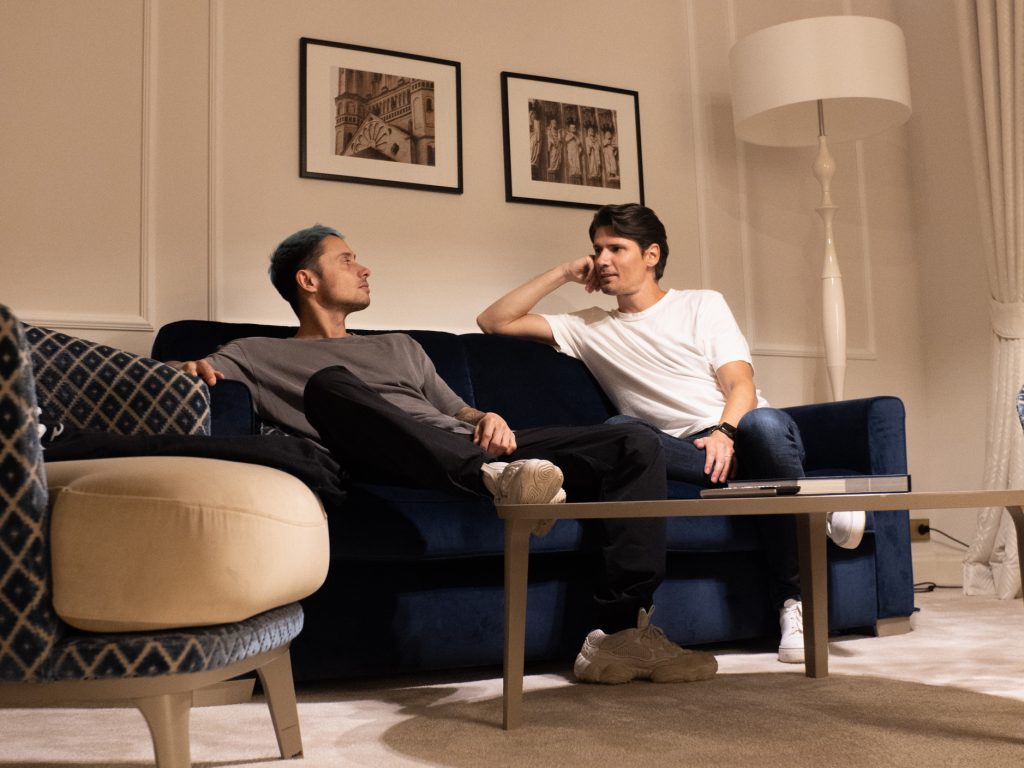 Promotional photo for "Wrong or Right (The Riddle)" which sees Bassjackers chilling on a blue velvet couch, looking at each other, wearing chilled clothes and just spending time with each other.