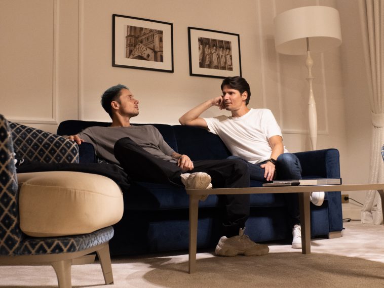 Promotional photo for "Wrong or Right (The Riddle)" which sees Bassjackers chilling on a blue velvet couch, looking at each other, wearing chilled clothes and just spending time with each other.