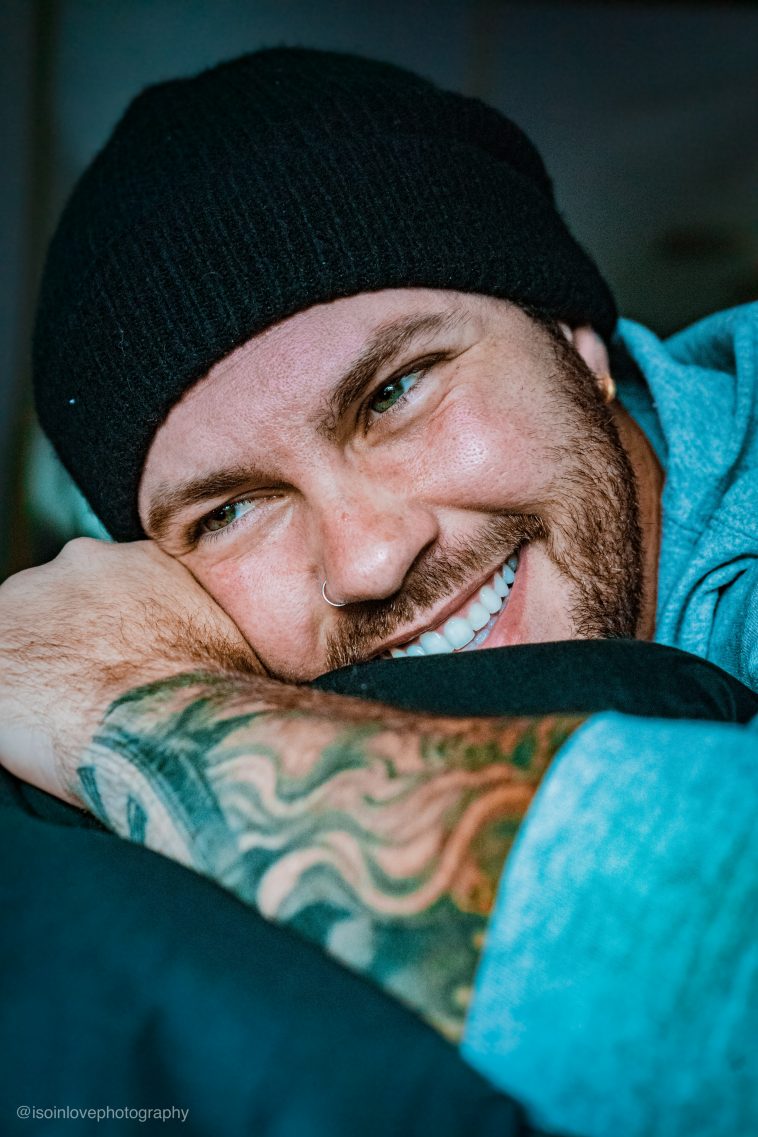 Promotional photo for "Dear Victoria" which sees a headshot of Carter Ray, who has the side of his head resting against his right arm. He is smiling and has a black beanie and a light blue shirt on.