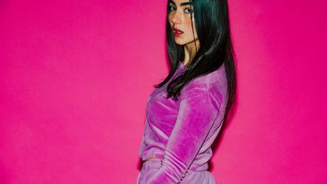 Promotional photo for "Lose U Now" which sees KEHLI with long black hair posing over her left shoulder in front of a bright pink background. She's wearing a pink velvet tracksuit.