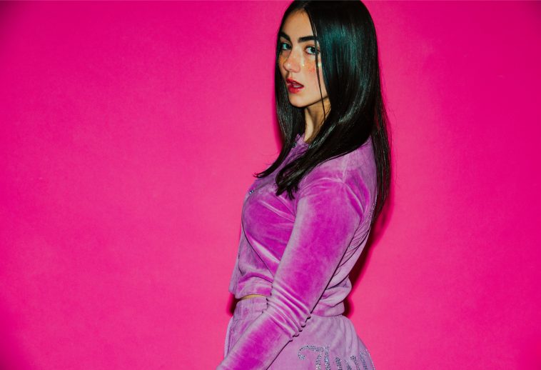 Promotional photo for "Lose U Now" which sees KEHLI with long black hair posing over her left shoulder in front of a bright pink background. She's wearing a pink velvet tracksuit.