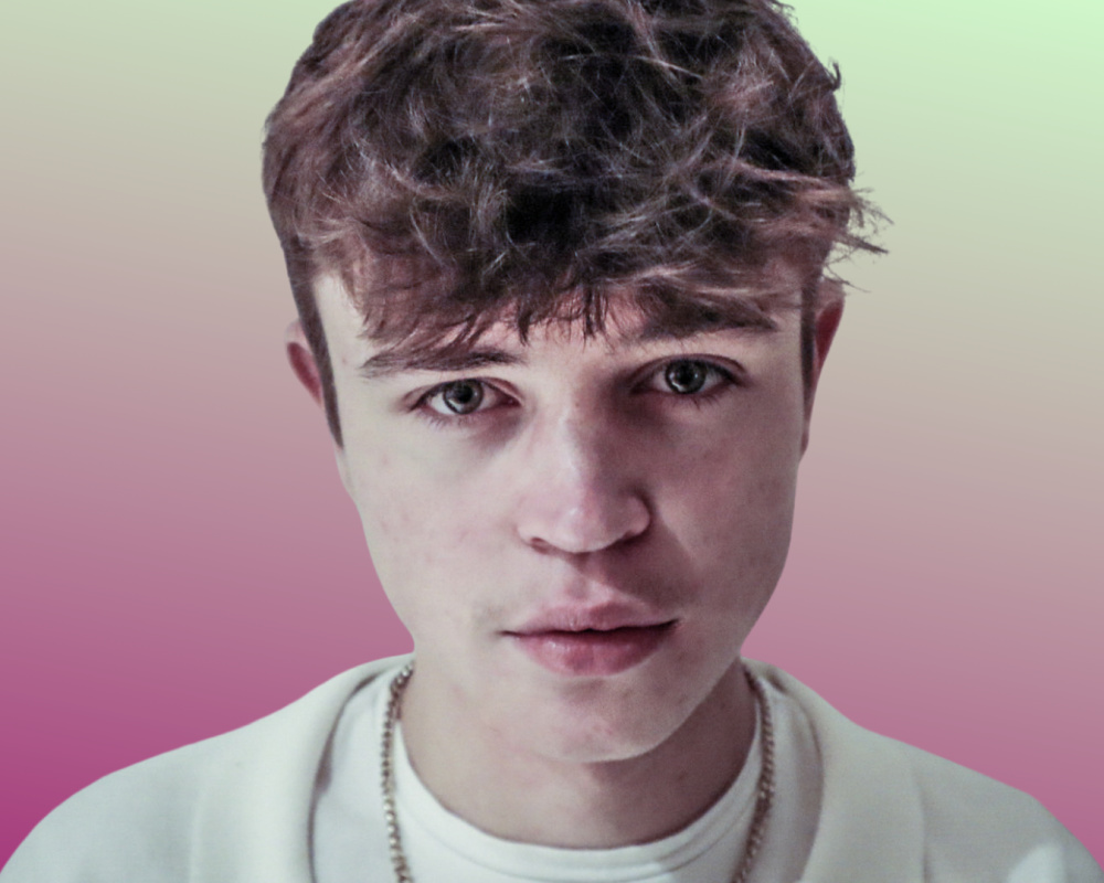 Promotional photo for "Little Bits" which is a headshot of Tom A. Smith who has brown hair with a curly fringe. He is wearing a pale green jacket over a white t-shirt, whilst the background is a pale-green-to-pale-pink ombre colour starting from the top