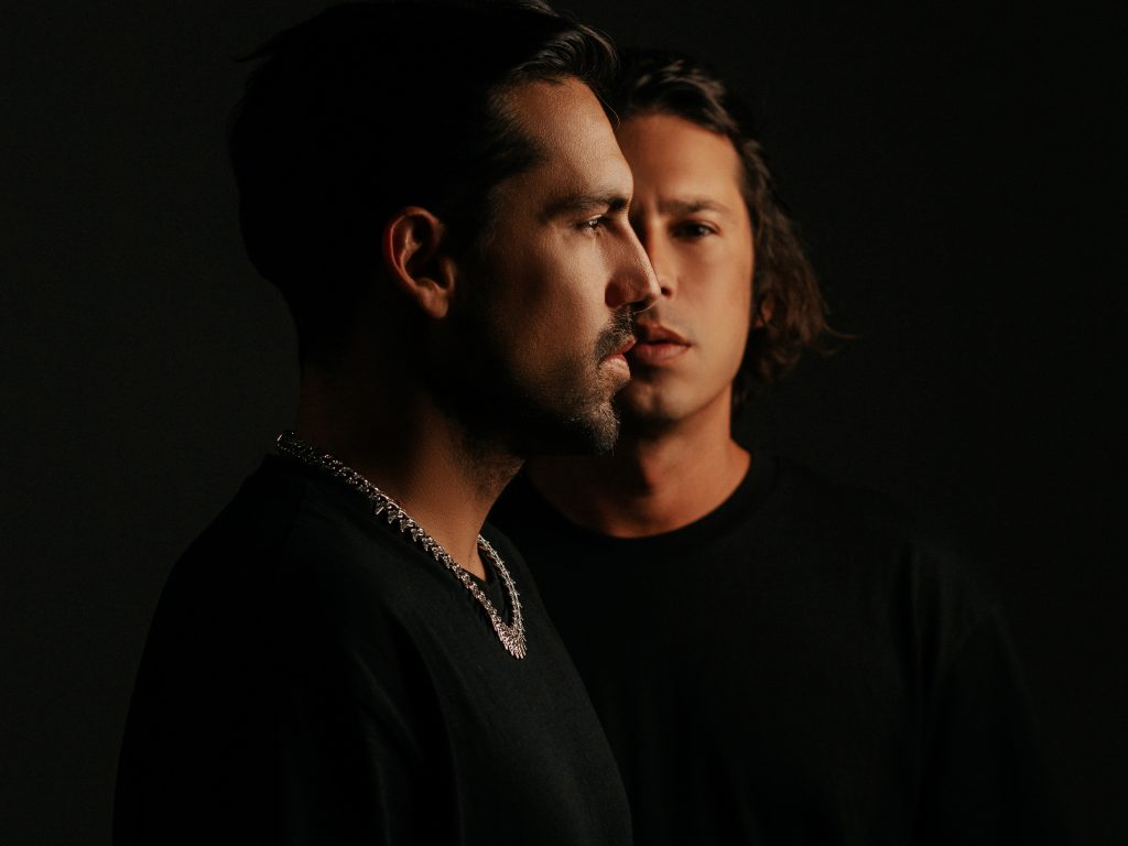 Promotional photo for "Bad For U" in collaboration with Mevil and Enigmix, which sees Chemical Surf posing in a photo studio with one of the brothers facing to the right and the other brother standing behind him and looking at the camera. Both of the DJs are wearing black t-shirts that blend into the background.