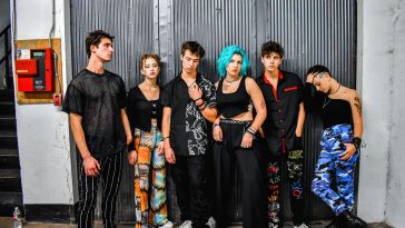 Promotional photo for "Blondie" which sees SM6 standing and posing against a metal garage door with all six band members wearing black, with some wearing different coloured tracksuit bottoms.