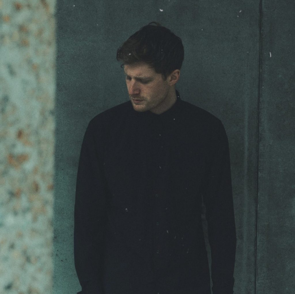 Promotional photo for "Over" by MARLOW which sees frontman Freddie Marlow leaning against a wall, wearing a black jumper and slightly looking to the left.