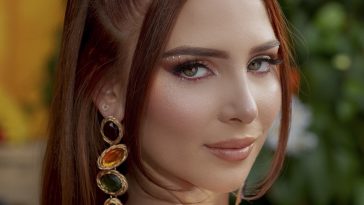 Promotional photo for "No Patience (No Tengo Paciencia)" which sees a head-shot of Chloe Jane looking over her shoulder with a three-gem earring dangling from her ear and her auburn hair tied back into two ponytails with two hair tendrils framing her face.