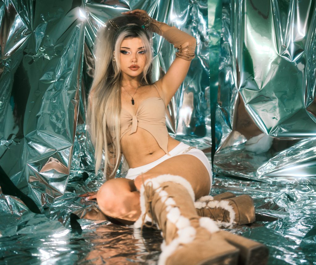 Promotional photo for "I Love You And It's Getting Worse" which sees Larissa Lambert in a metallic mirror room, wearing a nude-coloured bra and white hot pants and knee-high nude fur boots. Her white-grey-dyed hair fall around her beautiful face.