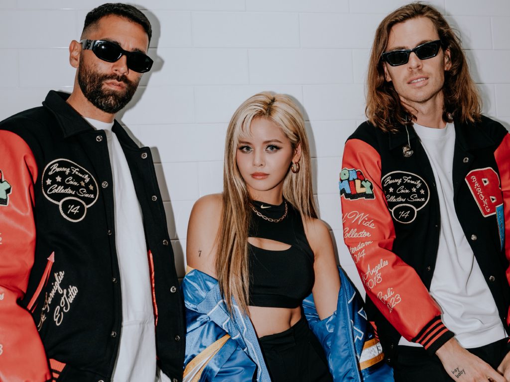 Promotional photo for "Cold Like Snow" which sees Sorn standing between the two guys of Yellow Claw. She has long blonde hair with her make-up on point with a denim jacket hanging off her shoulders and she's wearing a black particioned vest top. Yellow Claw are both wearing sunglasses, red and black varsity jackets over white t-shirts.