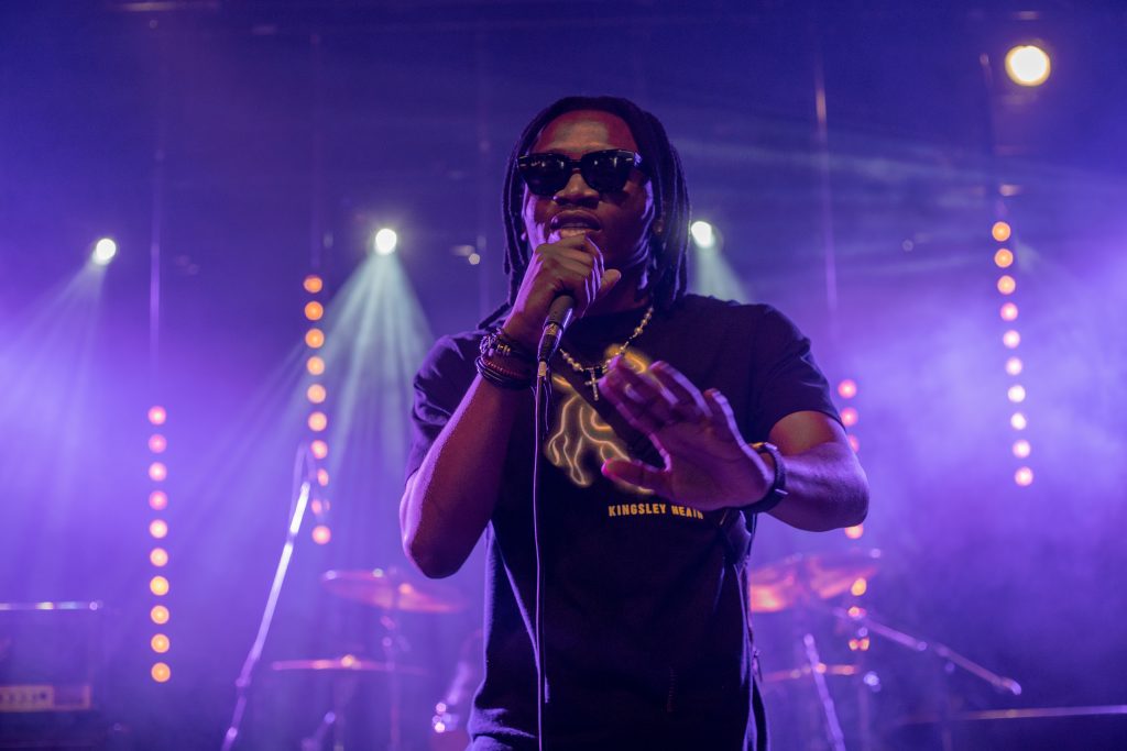 Promotional photo for "SUCCESS FEVER" which sees Tunde 2deep up on stage performing, with a microphone in front of his mouth and blue LED stage lights behind him.