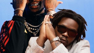 Promotional photo for "New Religion" which sees Olamide and Asake together against a blue background. Olamide is sitting down with his hands up to his head in a prayer sign, he is wearing a white jacket and dark shades. Asake is behind him with his arms up to his head with his hands in fists, showing off his bracelets. He is wearing a black jacket with red sleeve design, a few silver chain necklaces and some red-rimmed sunglasses, and he is grinning.