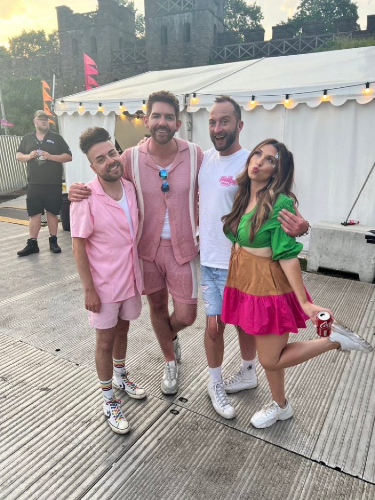 Photo of Scott McGlynn at Pride Cymru, posing with three other people, outside a white tent.