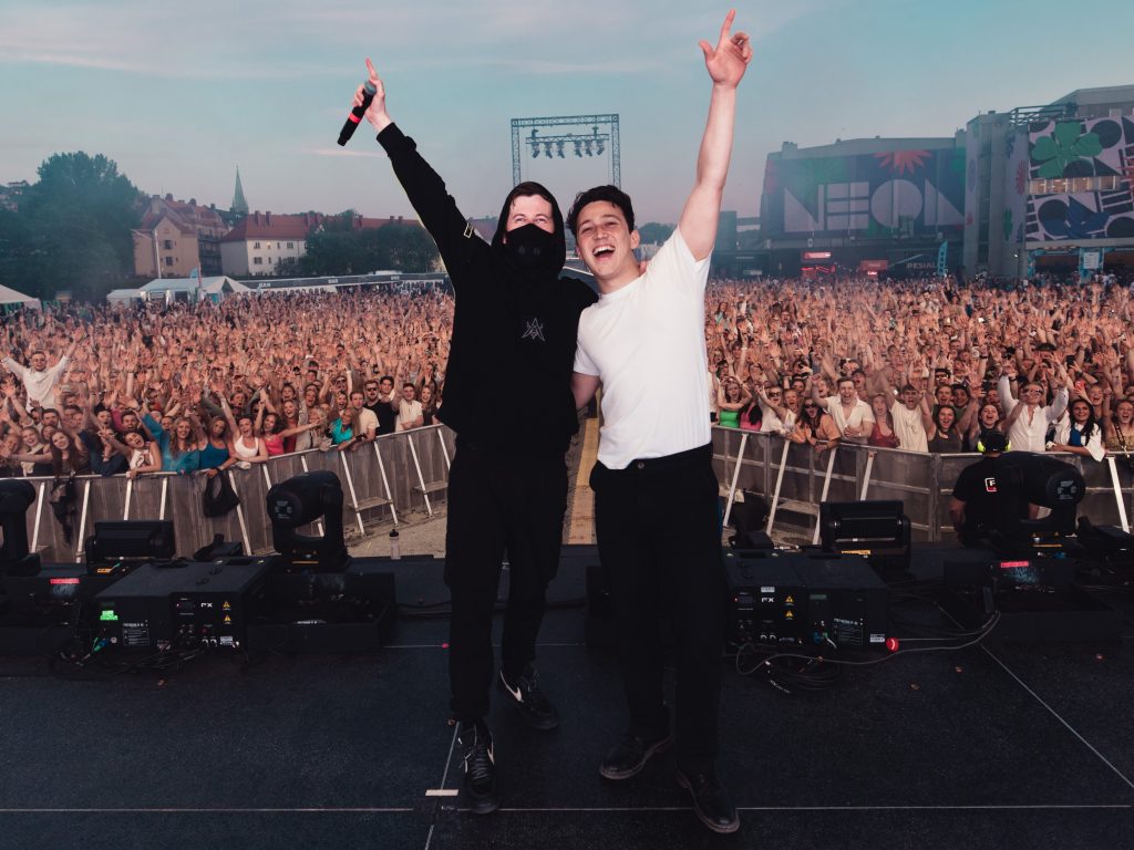 Promotional photo for "Endless Summer" which sees Alan Walker and Zak Abel on stage together with their back to the festival crowd as everyone poses for the camera. Alan Walker is dressed all in black and Zak Abel is wearing a white t-shirt with black joggers.