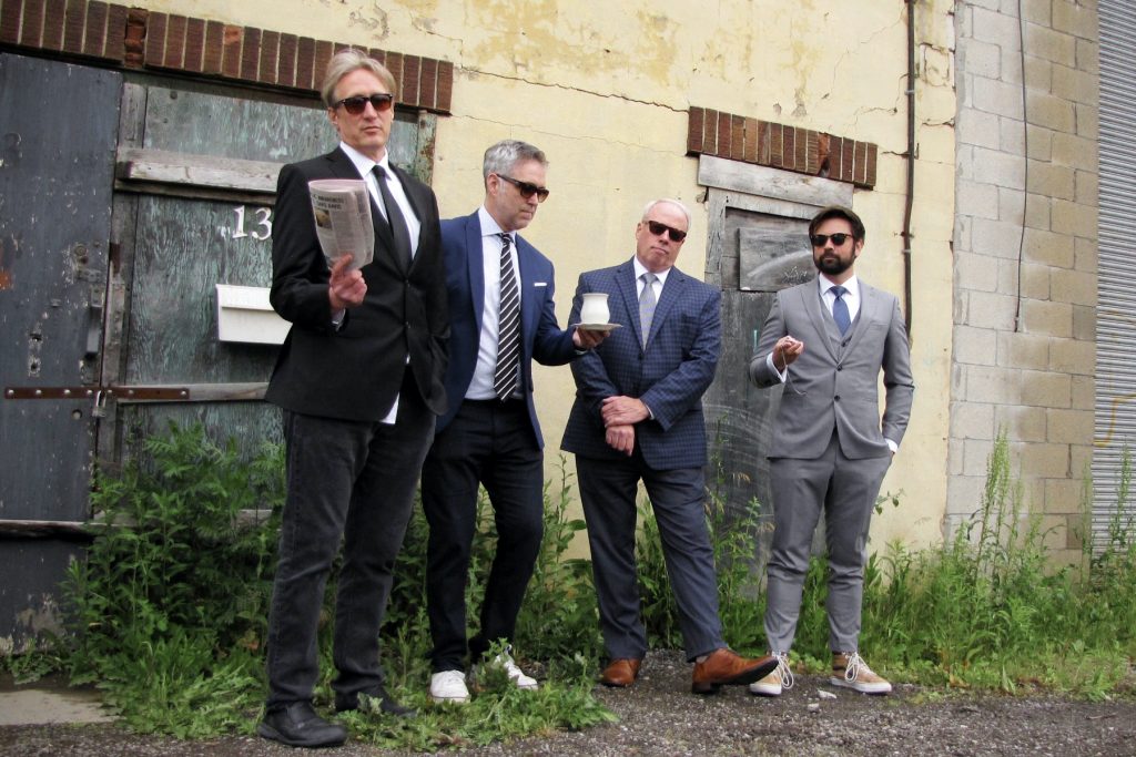Promotional photo for "Bled out at the Scene" which sees Elephants and Stars lining up for a band shot, with all four of them wearing suits with sunglasses.