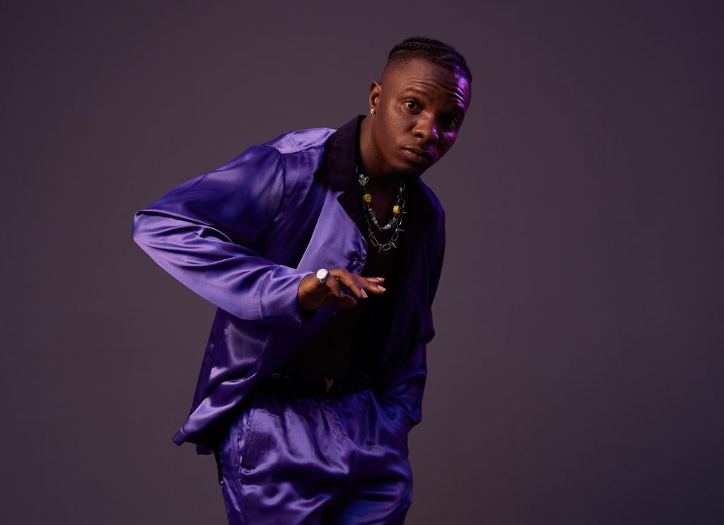 Promotional photo for "Wetin No Good (Remix)" in collaboration with Eltee Skhillz and DanDizzy, which sees Idahams posing at a photo studio with a purple background, and he's wearing velvet purple suit.