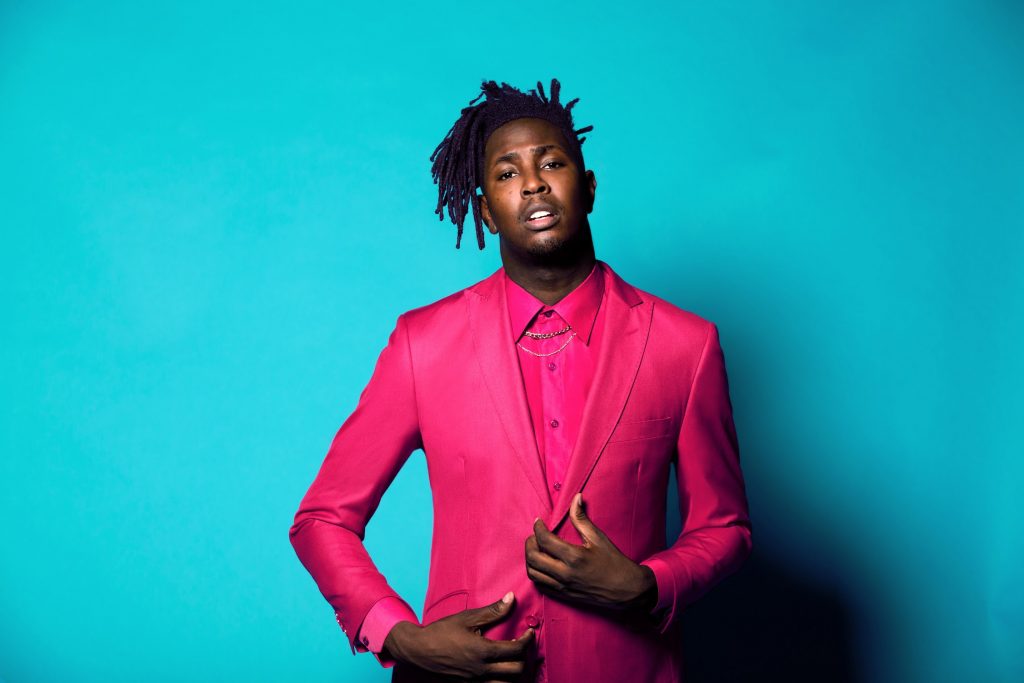 Promotional photo for "Summer Pack" EP which sees Mike Taylor dressed in a bright pink two-piece suit, standing against a bright blue background.