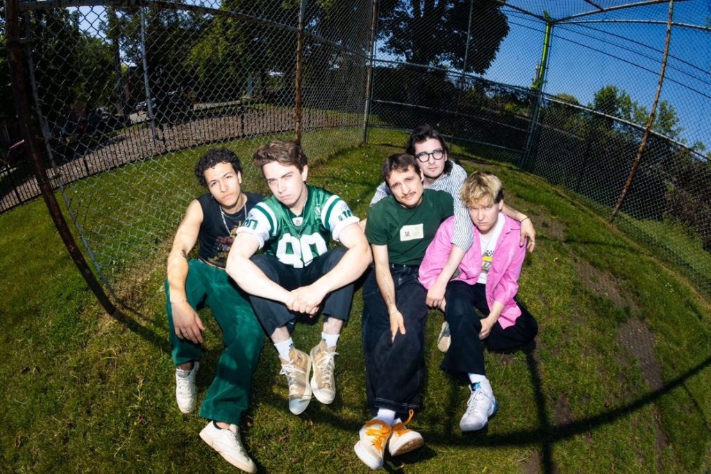Promotional photo for "Sad Sugar" which sees the band New Friends sitting on a patch of grass wearing sporty clothes.