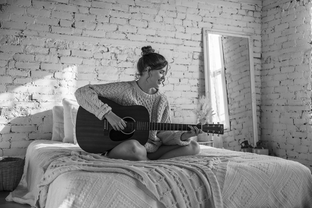 Promotional photo for "Here We Go Again" which sees a young woman, who is Victoria Staff, sitting cross-legged on a bed, playing her guitar. The photo was in black and white.
