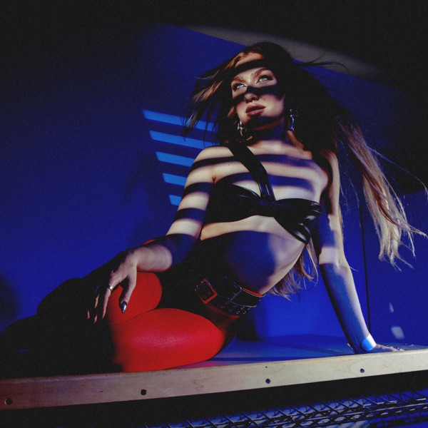 The single cover artwork for "HEARTBREAK ON REPEAT" which sees Olivia Lunny wearing red leather pants and a black bra as she lies on a metal counter with a wind machine flowing her hair behind her, in front of a blue background.