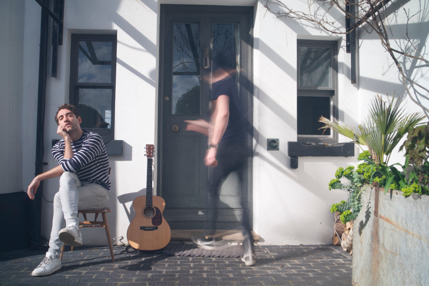 Promotional image for "C'est La Vie" which sees BANNERS sitting on the left side, in front of a house as a blurred man walks through the front door.