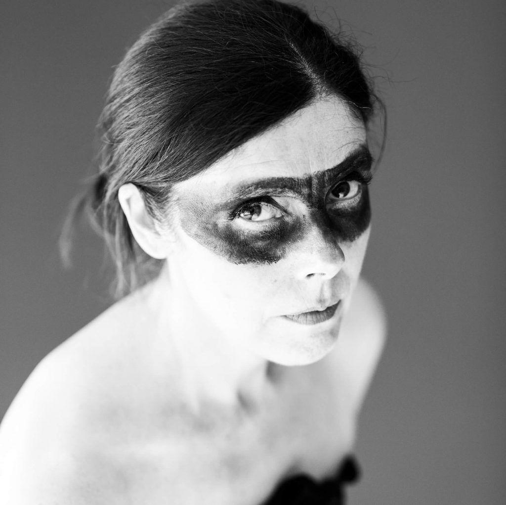 Black and white promotional photo for "Dark Horse" which is a headshot of Maria Wilman with her hair tied back and a black face-painted eye-mask marking on her face.