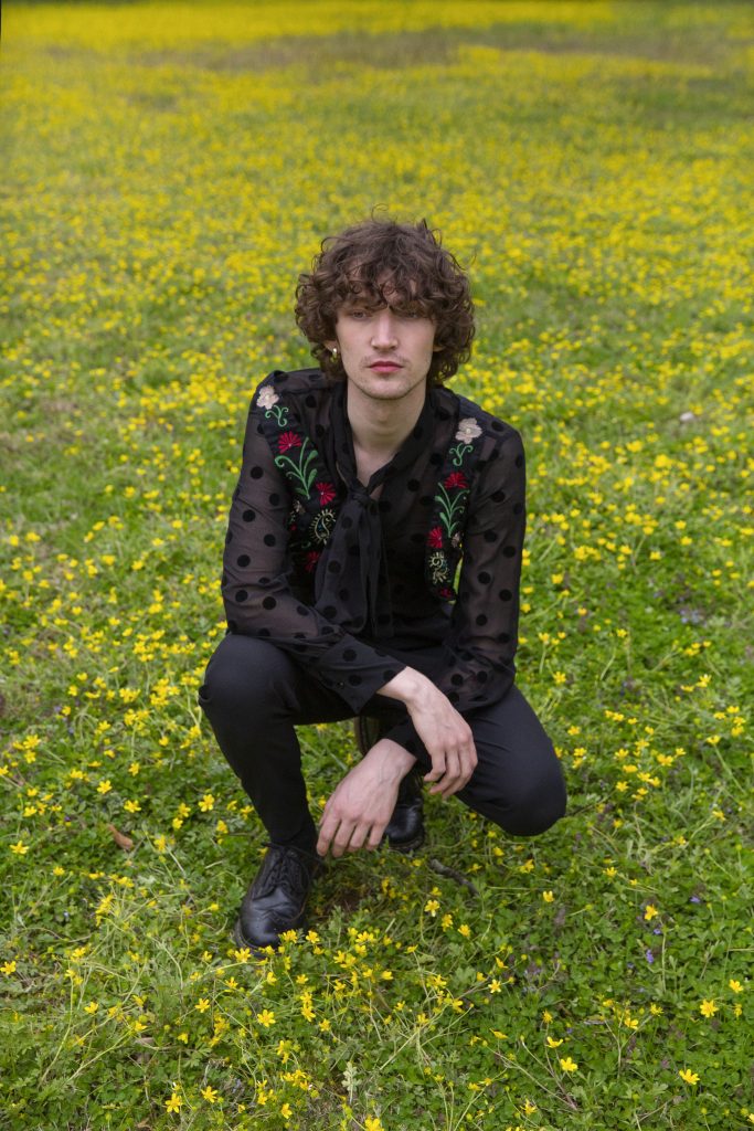 Promotional photo for "Star Crossed Lovers" which sees Otto Aday crouching in a field of grass.