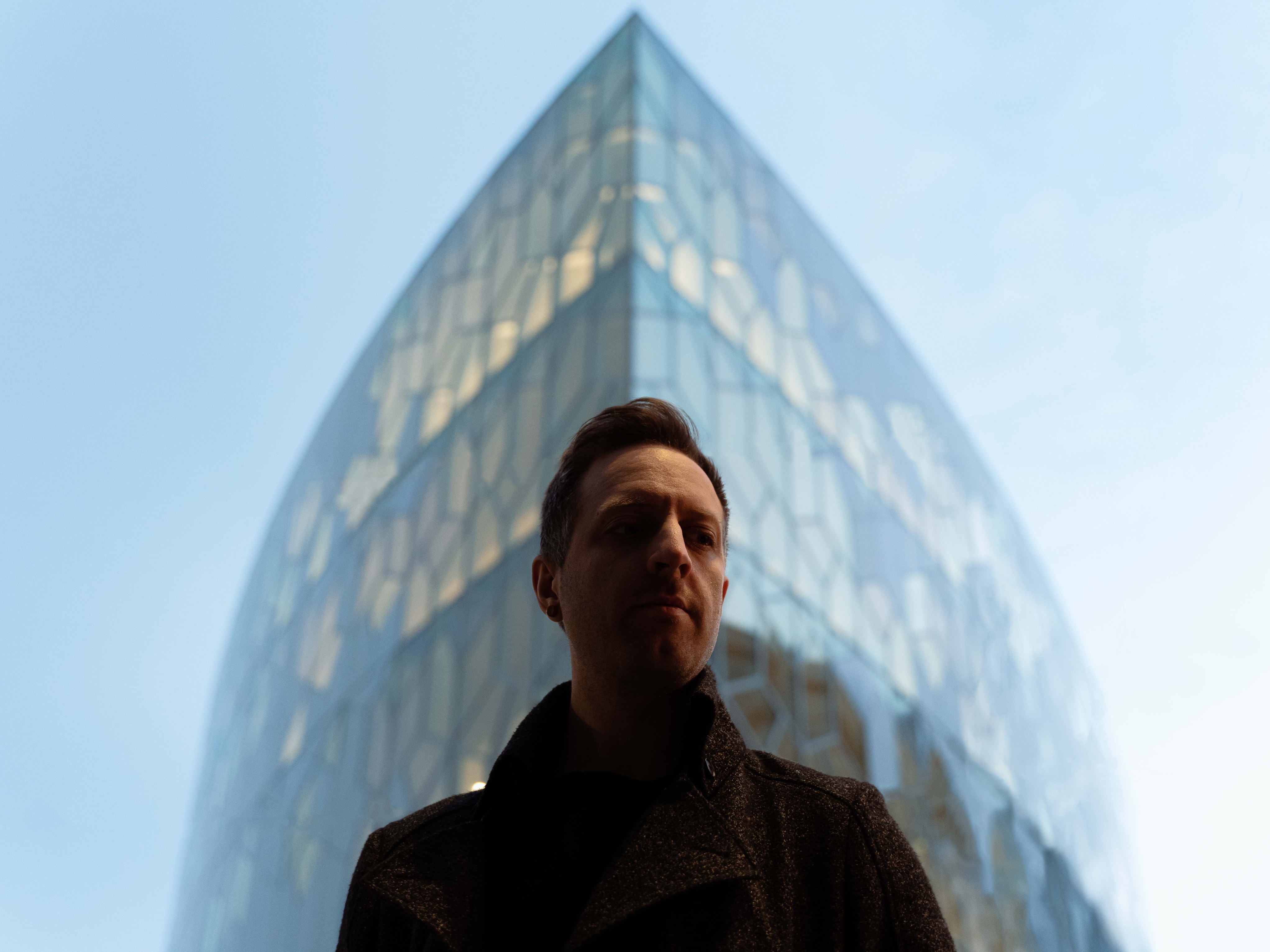 Promotional photo for "The Voyage" which sees Defunk standing in front of a tall glass corner building.