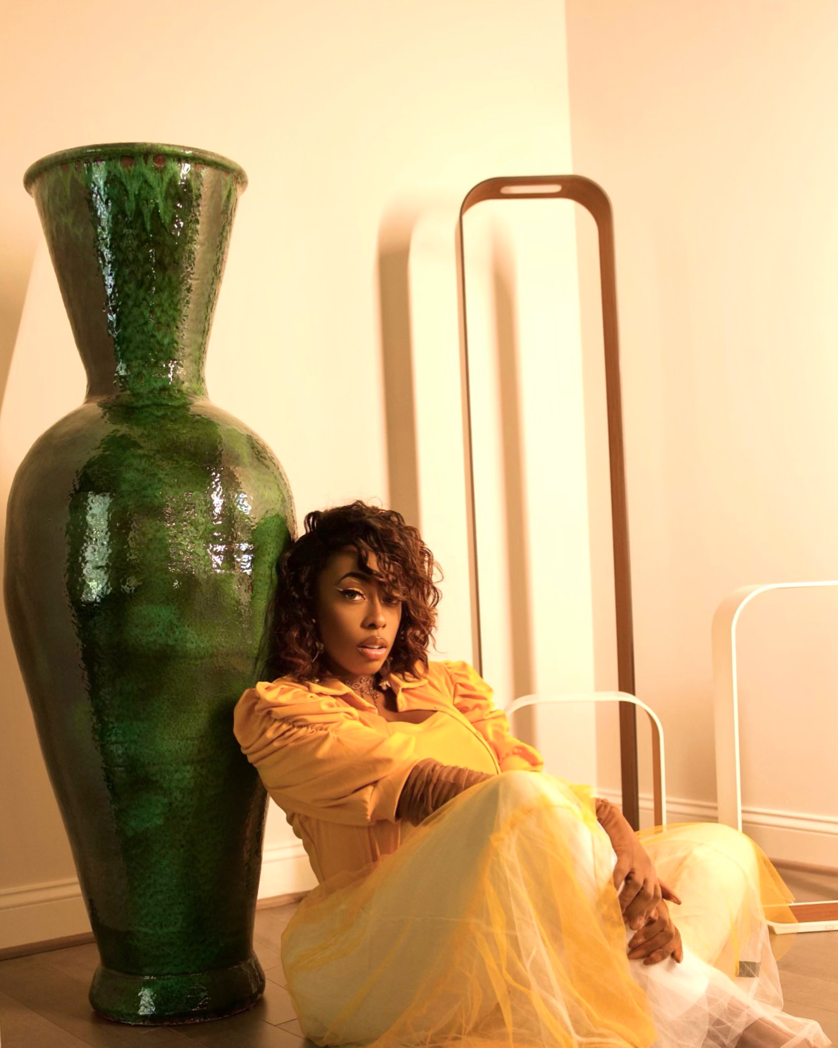 Promotional photo for "I Found It" which sees La Shana Latrice in a beautiful yellow dress, sitting on the floor and leaning against a huge gigantic green vase.