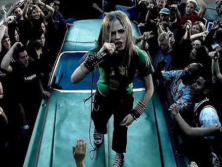 Still from the "Sk8er Boi" music video which shows Avril Lavigne on the bonnet of a car, singing the song.