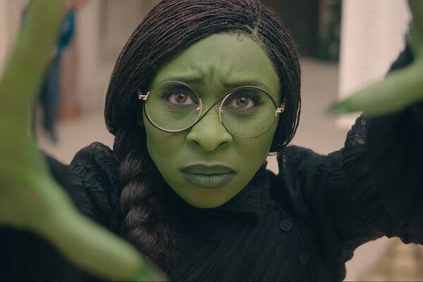 A woman with green skin holds her hands up toward the camera, a look of intense focus on her face.