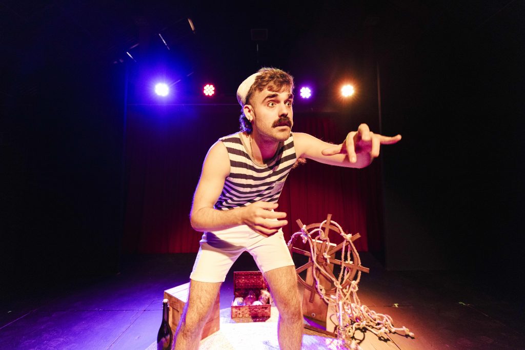 Darby James onstage performing Little Squirt, wearing a sailor hat, mid-song during the 2024 Edinburgh Fringe Festival